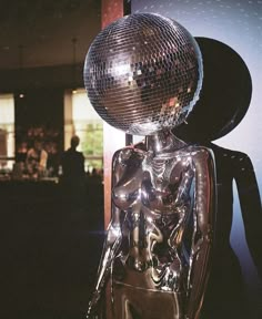 a shiny metal figure is standing in front of a large mirror ball on top of it