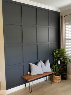 a room with a bench and some pillows on the floor in front of a wall