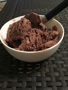 a bowl filled with chocolate ice cream sitting on top of a black table next to a knife