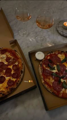 two pizzas sitting on top of cardboard boxes next to glasses of wine and candles