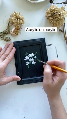 someone is painting flowers on a black frame