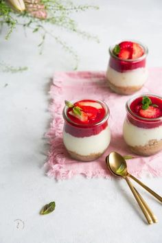 three small desserts with strawberries in them on a pink napkin and gold spoon