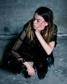 a young woman sitting on the ground with her hand to her face and looking down