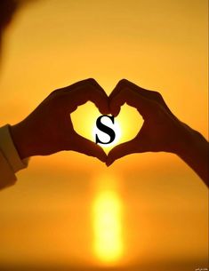 two hands making a heart shape with the letter s in front of an orange sunset