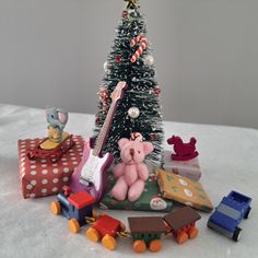 a teddy bear sitting next to a christmas tree with presents around it and a guitar