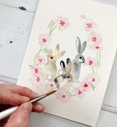 someone is painting two rabbits in a floral wreath with watercolor pencils on paper