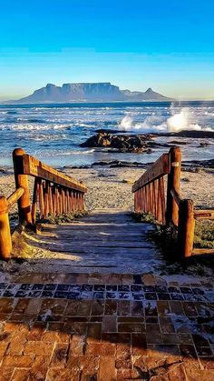 a wooden walkway leading to the ocean with mountains in the background