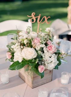 a wooden box filled with flowers and greenery on top of a white table cloth