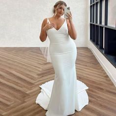 a woman in a white dress taking a selfie with her cell phone while standing on a wooden floor