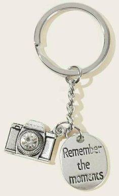 a silver keychain with a camera on it that says, remember the moments