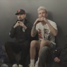 three men sitting next to each other in front of a wall with their hands together