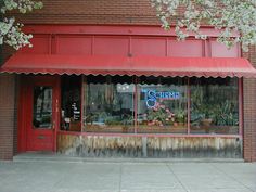 a store front with red awnings and flowers in the window