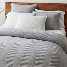 a bed with grey and white striped comforter set on top of the headboard