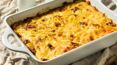 a casserole dish with meat and cheese in it on a table cloth next to a cup