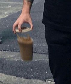 a man is holding a plastic cup with something in it while walking down the street