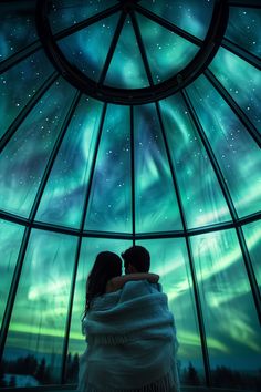 two people standing in front of a glass dome with the aurora lights on it's ceiling