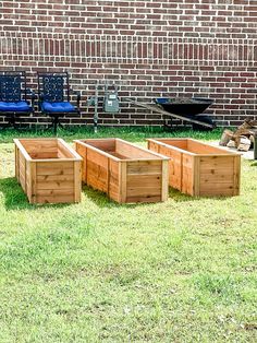 four wooden planters sitting in the grass next to a brick wall and blue chairs