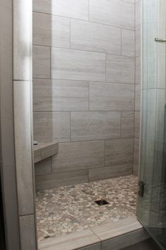 a walk in shower sitting next to a tiled wall and floor covered in pebbles on the ground