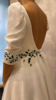 the back of a woman's wedding dress with green flowers on it and an open shoulder