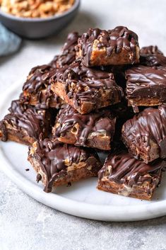 a white plate topped with chocolate covered brownies and pretzel crackers next to a bowl of nuts