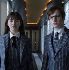 two young people dressed in suits and ties standing next to each other on a hallway