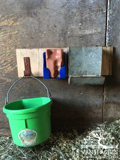 a green bucket sitting on top of hay next to a wooden block and pegs