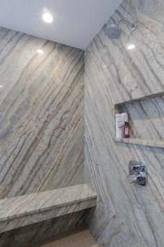 a bathroom with marbled walls and flooring, including a bench in the corner