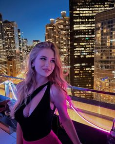 a woman standing on top of a roof in front of a cityscape at night