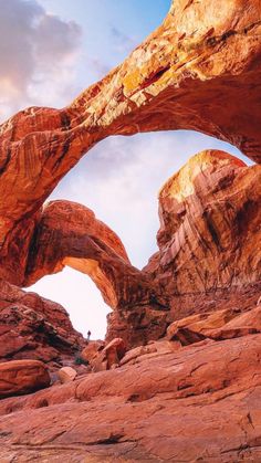 a large rock formation with a person standing under it in front of the rocks and sky