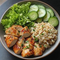 a bowl filled with rice, cucumber and chicken next to sliced cucumbers