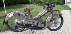 an old rusted motorcycle parked on the side of a road in front of a house