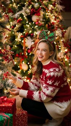 a woman is sitting next to a christmas tree with presents in front of her and smiling at the camera