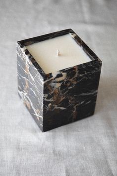 a marbled square candle holder with a single white candle in the center on a gray background