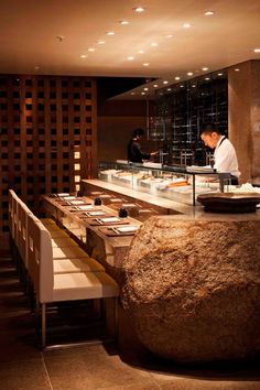 two chefs preparing food in a restaurant with large rocks on the counter and white chairs