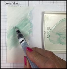 a person is holding a marker in front of some watercolor paper and a painting