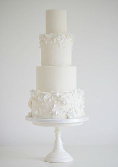 a three tiered white wedding cake with flowers on the top and bottom, sitting on a pedestal