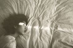 a black and white photo of a woman laying in bed with her head on the pillow