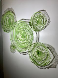 three glass vases sitting on top of a white wall with green flowers in them