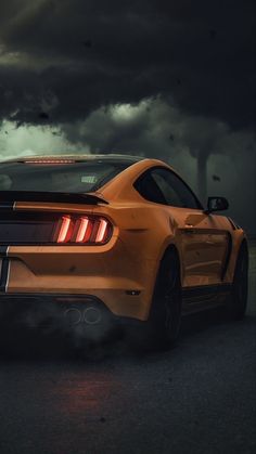 the rear end of a yellow sports car with dark clouds in the background