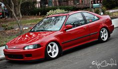 a red car is parked on the side of the road in front of a house