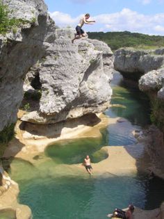 two people jumping off rocks into a river with clear blue water in the foreground