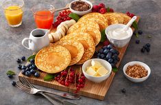 pancakes with butter, blueberries and berries on a cutting board next to orange juice