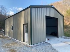 an empty garage with the door open and gravel in front of it, surrounded by trees