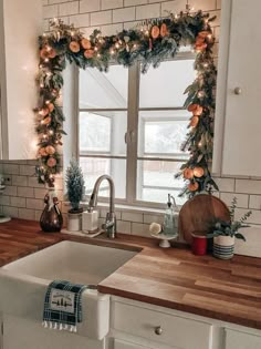 a kitchen decorated for christmas with orange flowers and greenery on the window sill