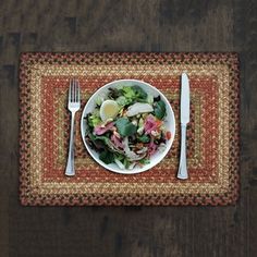 a white plate topped with salad on top of a table next to a fork and knife