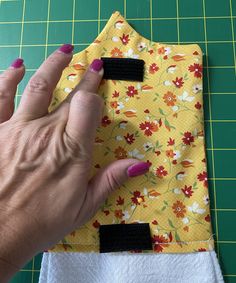 a woman's hand on top of a yellow flowered cloth with black pins