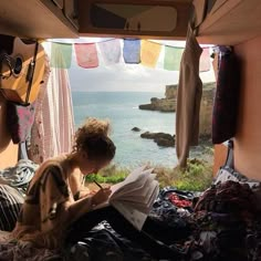 a woman sitting on top of a bed next to an open window with the ocean in the background