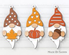 three wooden gnomes with autumn decorations hanging from the side on a white wood wall