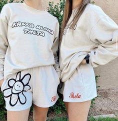 two young women standing next to each other wearing matching sweatshirts and shorts with flowers on them