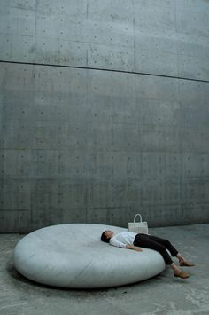 a person laying on top of a large round cushion in front of a building with concrete walls